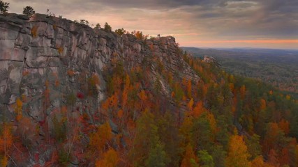 Autumn landscape: scenic cliffs covered by colorful forest, epic sunset in background. Aerial view 4K UHD