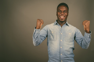 Young happy African man smiling with both arms raised against gr