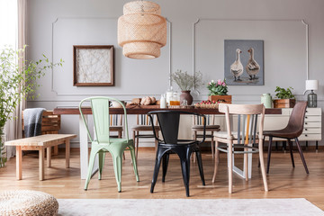 Different kid of chairs at table with flowers and food in rustic dining room interior with lamp and...