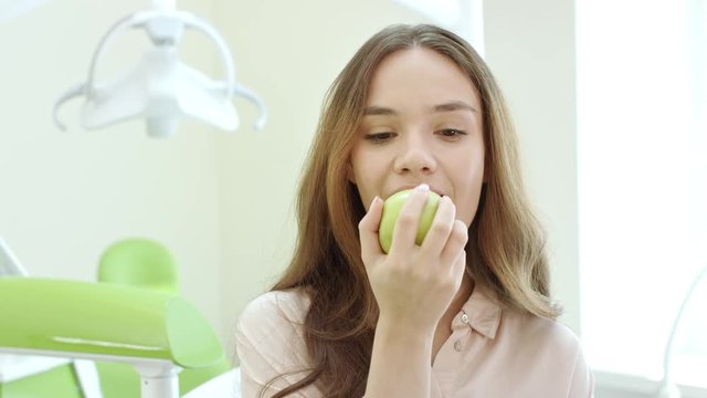 Portrait of happy woman eating apple in dental clinic. Smiling patient in dentist office. Laughing woman eat green apple in dental office. Healthy teeth concept