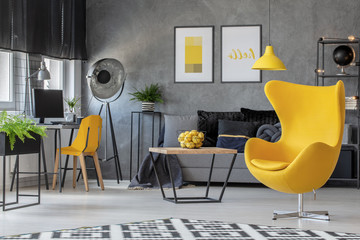 Industrial lamp in the corner of spacious scandinavian living room with yellow egg char, home office and coffee table with basket full of lemons, real photo