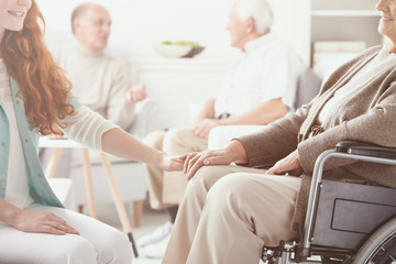 Friendly nurse helping happy disabled pensioner on wheelchair, nursing home concept