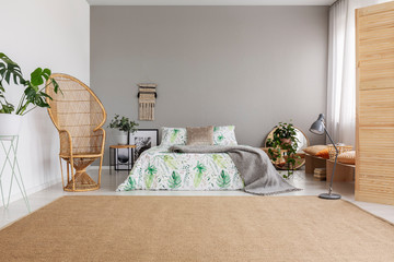 Beige natural carpet and wicker peacock chair in elegant bedroom interior with comfortable king size bed with leaf patterned bedding, real photo with copy space