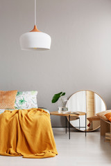 White chandelier above comfortable bed with yellow blanket in stylish bedroom interior, real photo with copy space on the empty grey wall