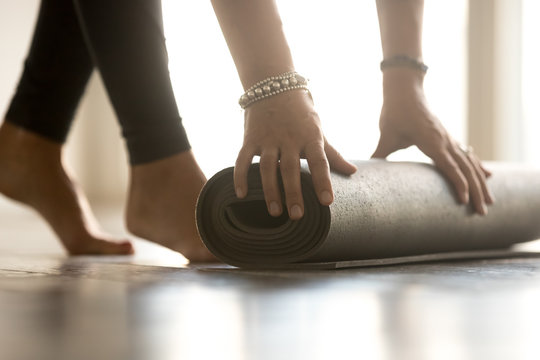 Fit woman rolling fitness, pilates or yoga mat before or after class in front of window in yoga studio club, gym or at home. Legs and body close up view. Healthy life, hobby, well being concept