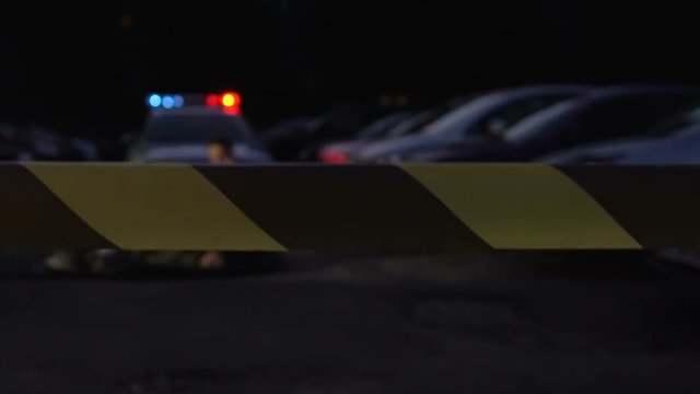 Police officer examining dead body of victim at crime scene surrounded with tape