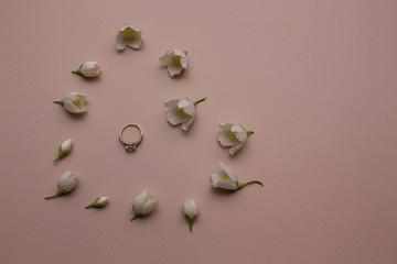 Jasmine flowers and one gold ring lie on wooden background in the shape of heart