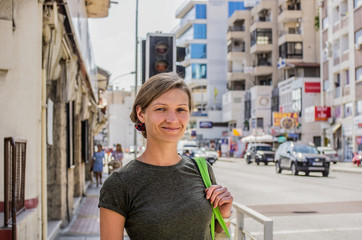 A young woman with a bag is standing at a crossroads at a traffic light