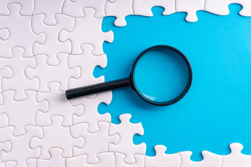 White jigsaw puzzle, Magnifier and missing pieces with selective focus and crop fragment. Business and education concept