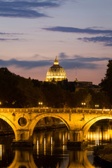 Fototapeta na wymiar Illuminated Dome of St. Peter's Basilica, bridge and the Tiber river at a beautiful sunset in Rome, Italy