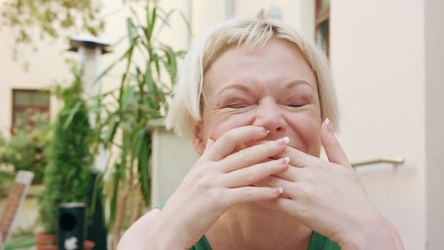A pretty young blonde woman wearing a green dress sitting outside laughing outloud. Close-up shot
