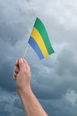 Hand holding Gabon flag high in the air, with a stormy, cloudy sky