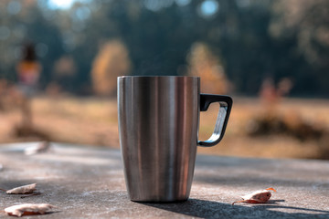 A cup of tee standing on a outdoor desk in a beautidul autumn scenery. coffee, tee, fall, landscape, cup, outdoor drink;