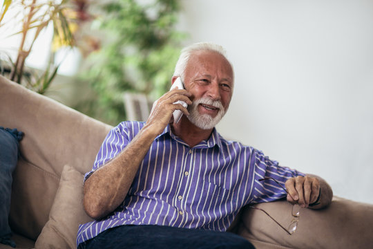 Senior man chatting on a mobile phone while relaxing on a sofa in his living room