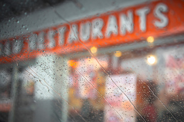 Drizzle rain drop on glass with fast food restaurant, burger cafe store at night blur bokeh abstract background.