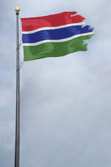 Worn and tattered Gambia flag blowing in the wind on a cloudy day