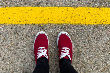 Red sneakers in front of the yellow line. Safety concept - obrazy, fototapety, plakaty
