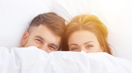Funny couple in love lying in the bed hiding themselves under