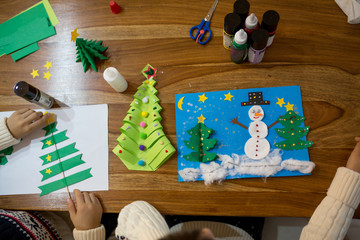 Top view of child, doing snowman and winter tree. Scissors, glue stick, pencil, markers, paper...