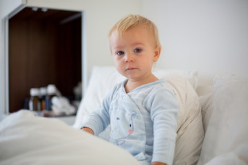 Fototapeta premium Little toddler boy in pajama with running nose and fever, lying in bed, mom taking care of him