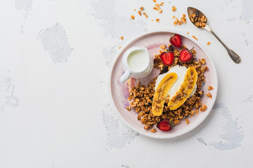 Oatmeal granola with yoghurt, fresh strawberries and banana, chia seeds, sunflower and honey in white ceramic plate on light background. Top view.
