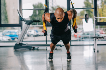 young african american sportsman exercising on fitness straps at gym