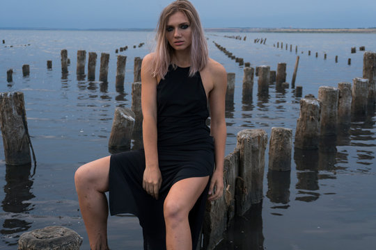 Portrait of Blonde Caucasian Girl in a Healthy Black Mud in old Firth with Wooden Posts for Salt Production
