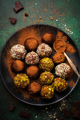 Variety of homemade dark chocolate truffles with cocoa powder, pistachios, almonds in dark brown background texture. Top view, copy space.
