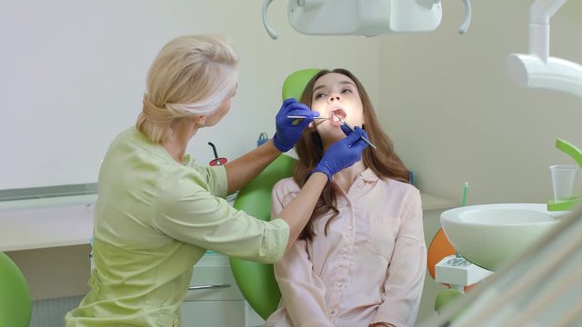 Dental caries treatment in dentist office. Young woman with open mouth in dentist chair. Female dentist treating sick tooth. Dental medicine practice concept. Professional stomatology assistance