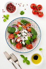 Tomatoes, spinach leaves, red onions and feta cheese salad on a light ceramic plate. Selective focus. Top view.