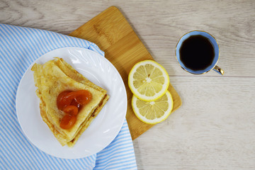 Delicious hot pancakes with apricot jam on a white plate and tea with lemon.