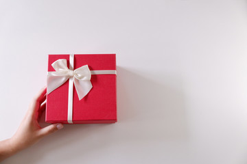Close-up women hands sending red gift box with white ribbon on white background.
