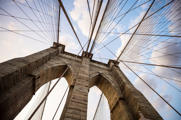 Close-up abstract view of the stone tower arch and steel suspension cables of the Brooklyn Bridge under scenic sunset skies