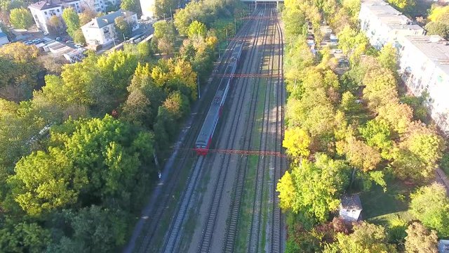 A aerial shot of a passenger electric train in moving towards in city, Passenger train rides near house under bridge. Railways Russia Krasnodar. Aerial video view from above train 4k.