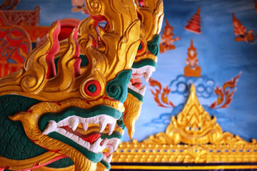 Carved wooden golden dragon statue in a Thai temple with Buddhist scene painted on a wall blurred in the background