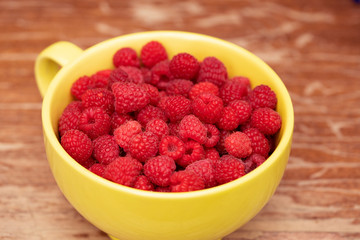 Close up of ripe raspberries in a big yellow cup on a wooden background