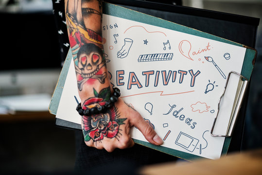 Tattooed hand holding a creativity clipboard