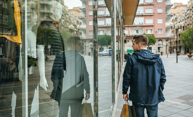 Young man with shopping bags walking in front of a clothing store