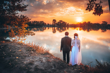 Bride and groom looking at autumn orange sunset in wedding day