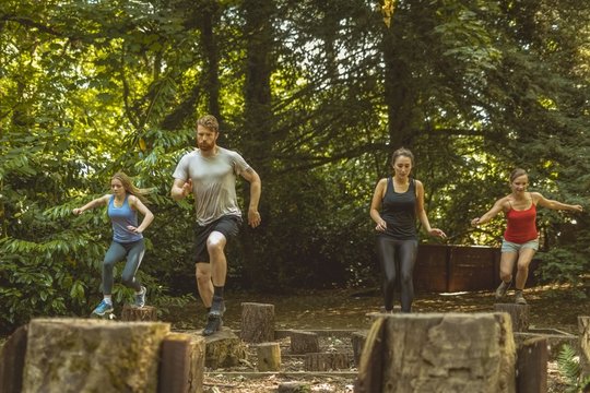 Group of people jumping over tree stumps during obstacle course