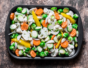 Raw ingredients for cooking vegetarian lunch - seasonal vegetables - brussels sprouts, carrots, cauliflower, pumpkin, onion, sweet pepper on a baking tray on a wooden background, top view