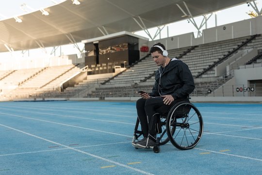 Disabled athlete listening to music on smartphone in stadium - Powered by Adobe