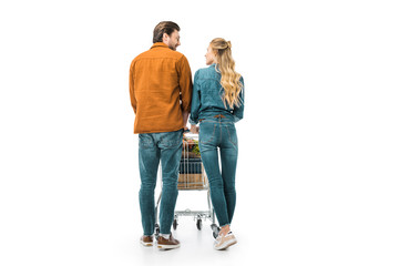 rear view of couple carrying shopping trolley with products and looking at each other isolated on...