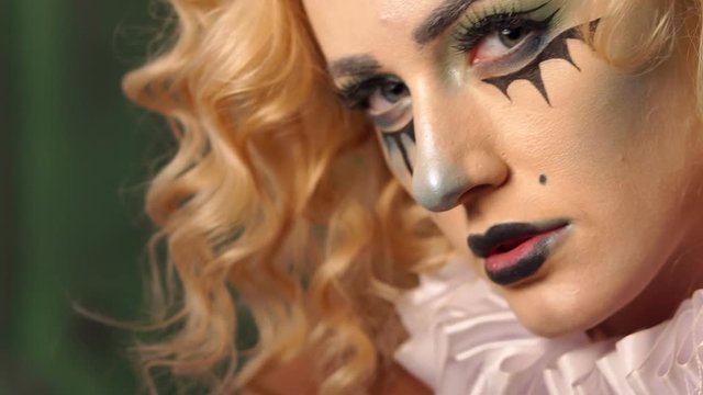 Close-up portrait of an excited blonde woman with make-up in halloween. Eerie makeup on the face of a girl with black streaks and black lips. Fashionable makeup for Halloween party, horror and mystery