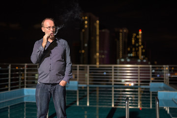 Mature man smoking electronic cigarette on the rooftop swimming 
