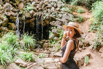 Young woman tourist with straw hat looking at the waterfall in nature park