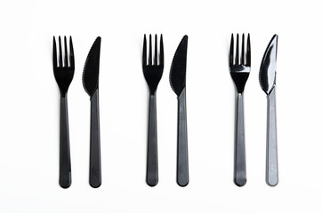 Clean plastic black forks and knives on white background. Disposable dishes, environmental pollution. Top view, flat lay.