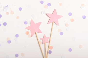 Pink stars on a stick topping on white background with confetti, pastel colors. Children's holiday, new year. Top view, flat lay.