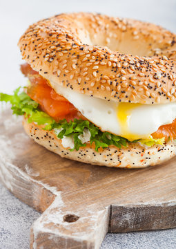 Fresh healthy bagel sandwich with salmon, ricotta and soft egg on vintage chopping board on white kitchen table background. Healthy diet food. Close up