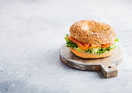 Fresh healthy bagel sandwich with salmon, ricotta and lettuce on vintage chopping board on stone kitchen table background. Healthy diet food. Space for text